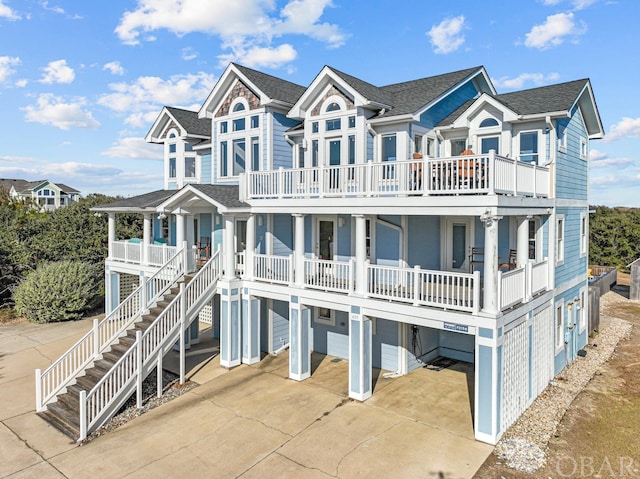 beach home featuring a porch, concrete driveway, a balcony, a residential view, and stairs