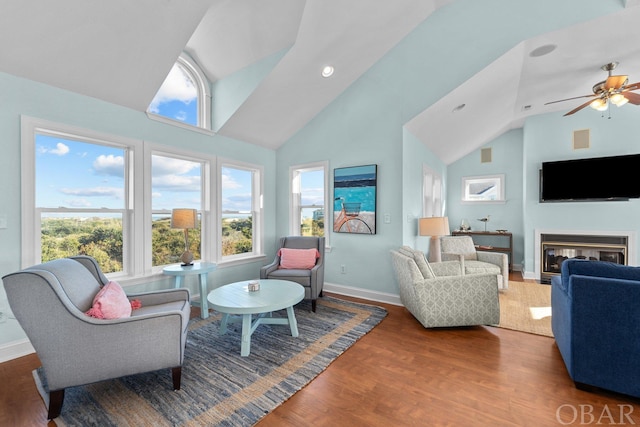 living room with a glass covered fireplace, ceiling fan, wood finished floors, high vaulted ceiling, and baseboards