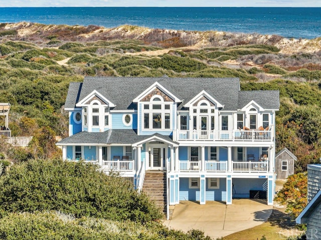 view of front of property featuring stairs, a water view, driveway, and roof with shingles