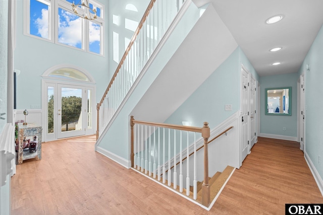 hallway with baseboards, a towering ceiling, stairs, light wood-style floors, and recessed lighting