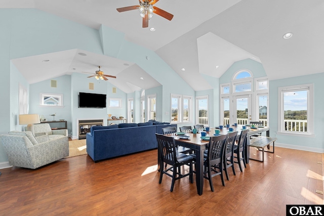 dining space featuring high vaulted ceiling, a glass covered fireplace, plenty of natural light, and wood finished floors