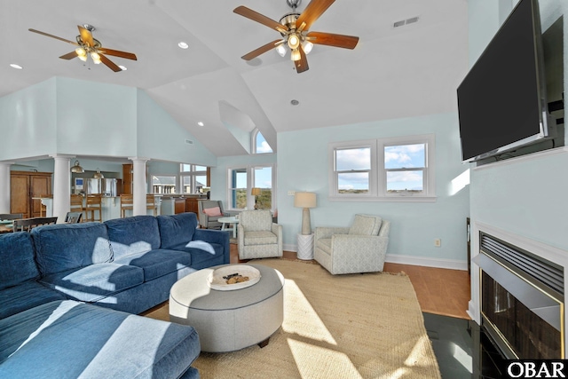 living room with visible vents, a fireplace with flush hearth, a ceiling fan, light wood-type flooring, and ornate columns