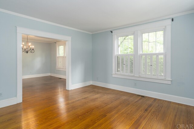 unfurnished room featuring baseboards, visible vents, wood finished floors, crown molding, and a notable chandelier
