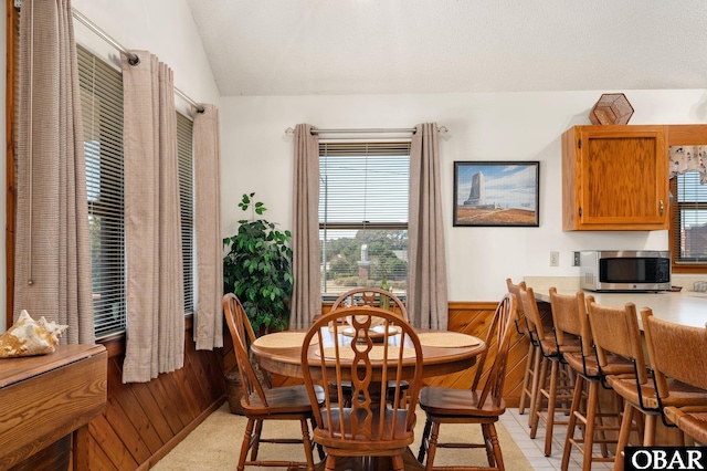 dining space with lofted ceiling, a wainscoted wall, and wood walls