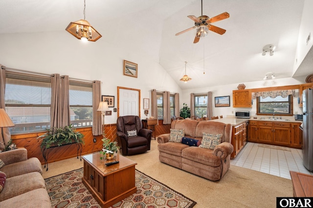 living room featuring a wainscoted wall, light tile patterned floors, light carpet, ceiling fan, and high vaulted ceiling