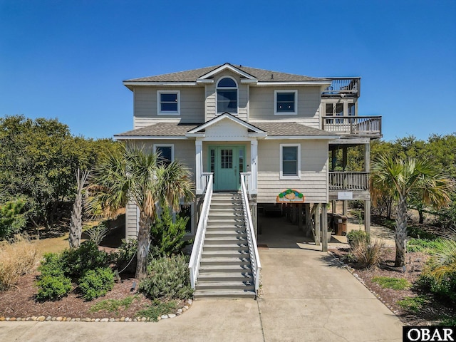 coastal home featuring a carport, roof with shingles, driveway, and a balcony