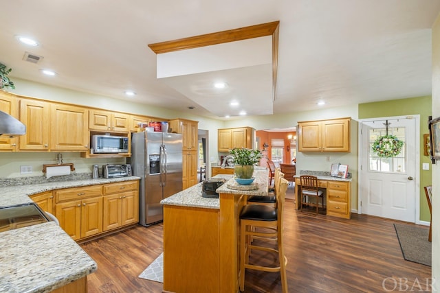 kitchen featuring visible vents, dark wood finished floors, a kitchen breakfast bar, a center island, and stainless steel appliances