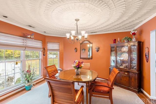 dining room featuring visible vents, ornamental molding, wood finished floors, a chandelier, and baseboards