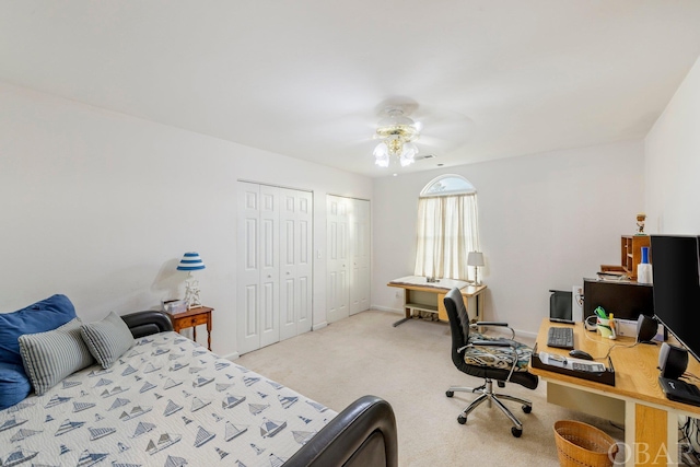 bedroom with light carpet, baseboards, a ceiling fan, and multiple closets