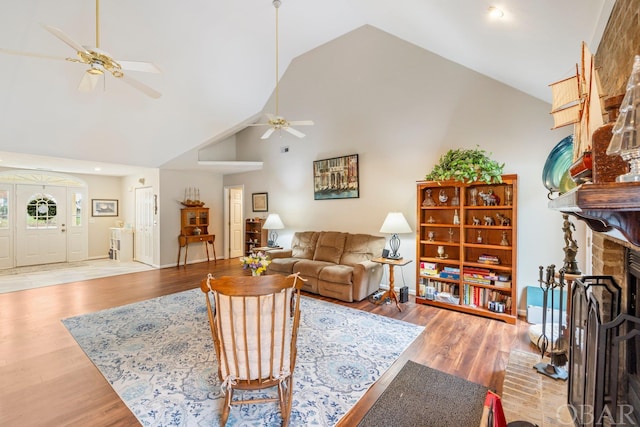 living room with high vaulted ceiling, a ceiling fan, baseboards, light wood-type flooring, and a brick fireplace