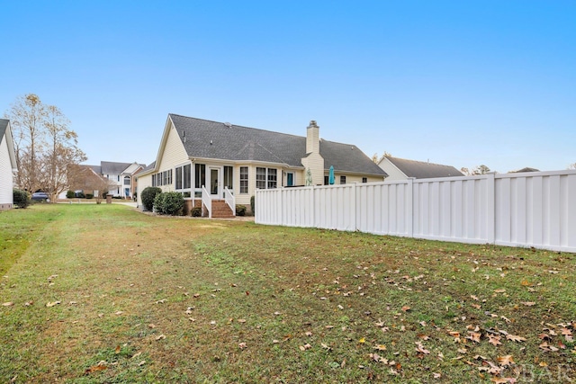 back of house with a sunroom, a chimney, fence, and a lawn