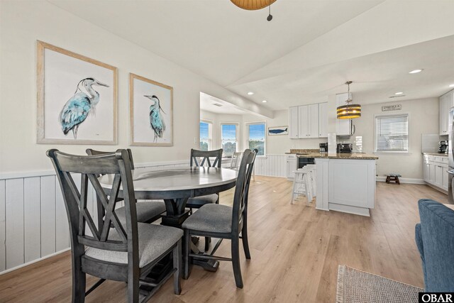 dining room featuring light wood-style floors, lofted ceiling, wainscoting, and plenty of natural light