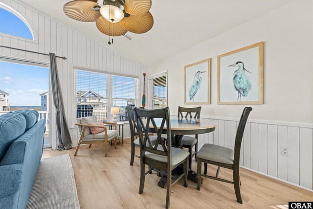 dining area with wainscoting, vaulted ceiling, and light wood finished floors