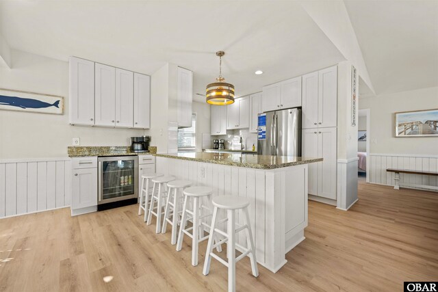 kitchen with wainscoting, wine cooler, a kitchen island, freestanding refrigerator, and white cabinetry