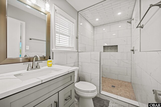 bathroom with toilet, tiled shower, and vanity