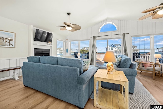 living area featuring lofted ceiling, light wood finished floors, a fireplace, and a ceiling fan