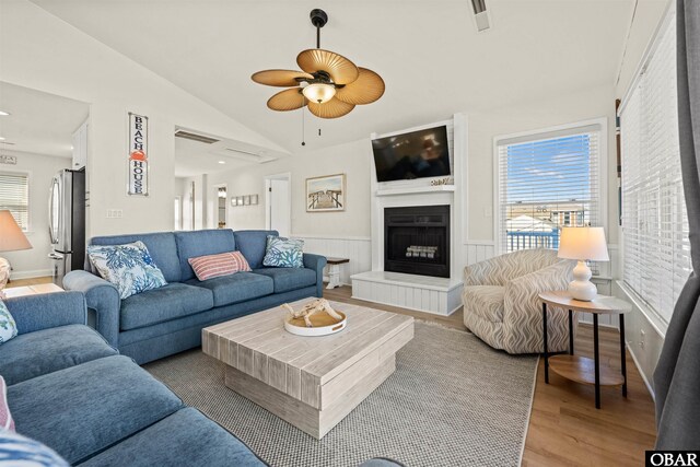 living area featuring lofted ceiling, light wood-style floors, a fireplace, and a healthy amount of sunlight