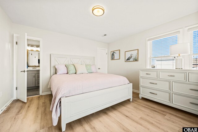 bedroom with light wood-style floors, baseboards, a sink, and ensuite bathroom