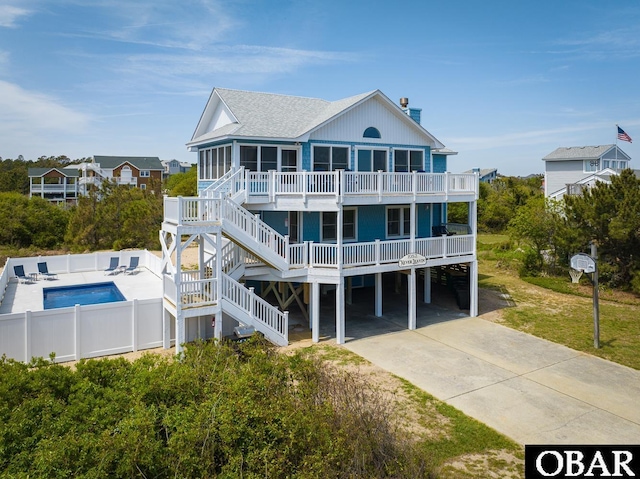 rear view of property featuring concrete driveway, a sunroom, fence, a carport, and stairs