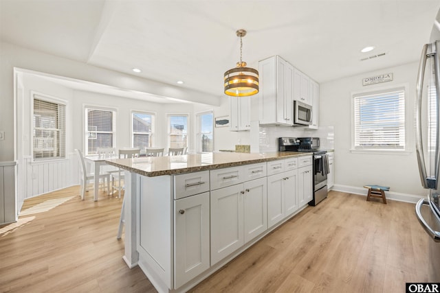 kitchen featuring visible vents, appliances with stainless steel finishes, a peninsula, light wood-style floors, and a wealth of natural light