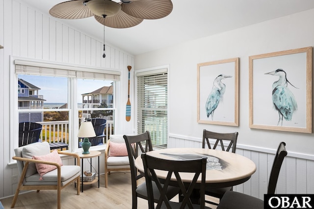 dining room with a wainscoted wall, light wood-type flooring, a wealth of natural light, and a ceiling fan