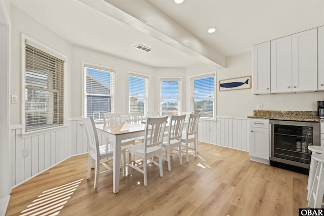 dining area featuring beam ceiling, a wainscoted wall, visible vents, light wood-style floors, and beverage cooler