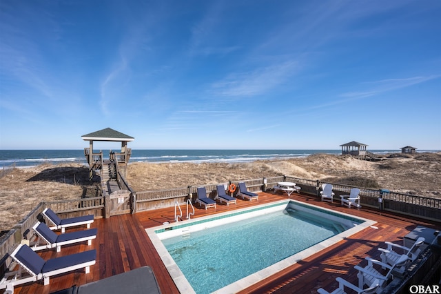 view of pool featuring a fenced in pool, a deck with water view, and a beach view