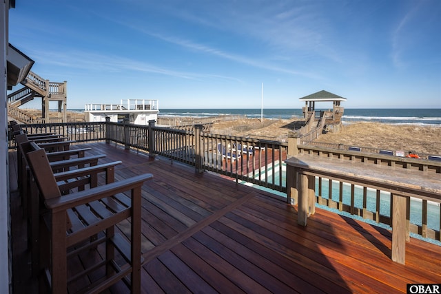 wooden terrace featuring a beach view and a water view