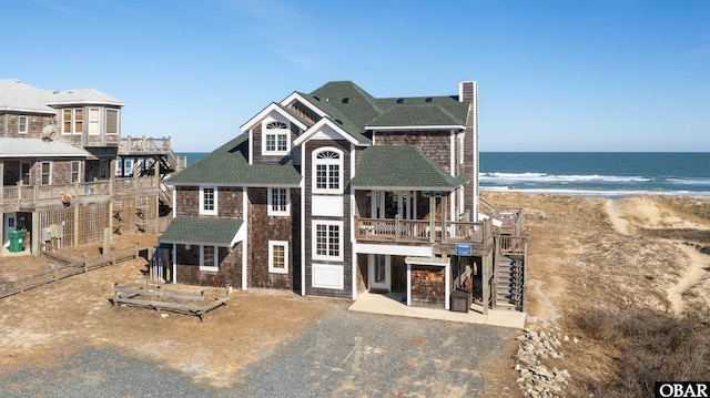 view of front of property with a shingled roof, a water view, and a view of the beach