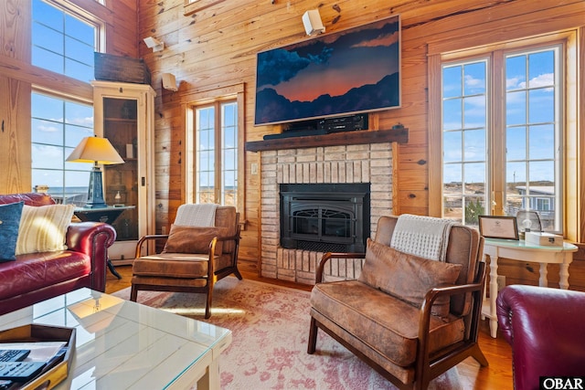 living area with wood walls, light wood-style flooring, a fireplace, and a high ceiling