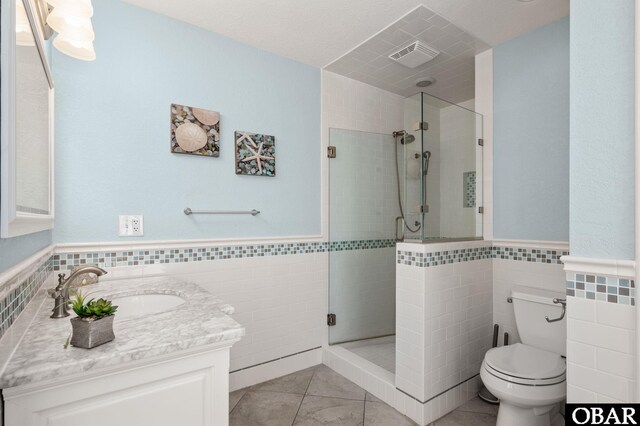 full bathroom with toilet, visible vents, vanity, tile walls, and a shower stall