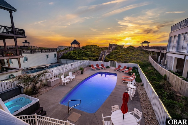 pool at dusk with a fenced in pool, an outdoor hot tub, a fenced backyard, and a patio