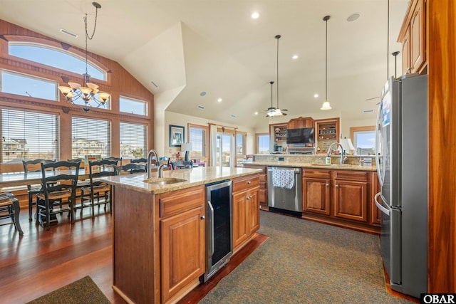 kitchen with a sink, brown cabinets, an island with sink, appliances with stainless steel finishes, and wine cooler