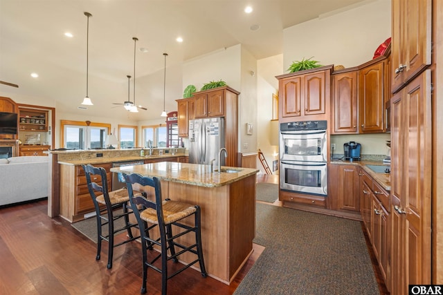 kitchen with a peninsula, a kitchen island with sink, a sink, open floor plan, and appliances with stainless steel finishes