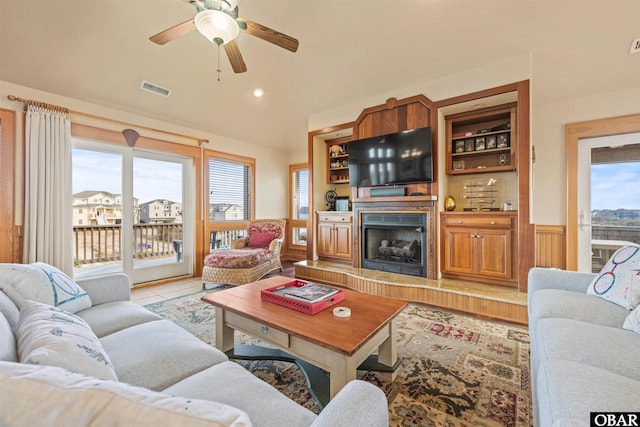 living room featuring vaulted ceiling, a ceiling fan, a fireplace with raised hearth, light tile patterned floors, and visible vents