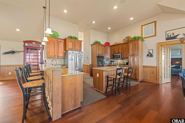 kitchen with high vaulted ceiling, wainscoting, brown cabinets, a breakfast bar, and appliances with stainless steel finishes