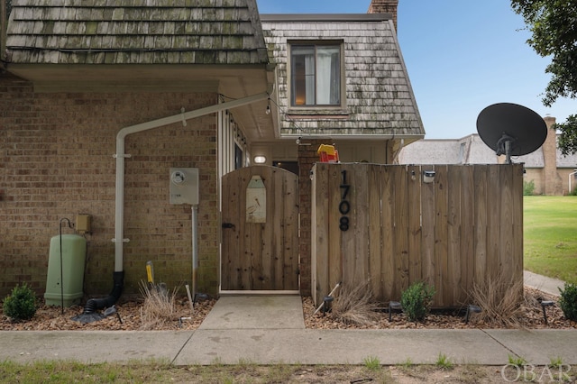 exterior space featuring a gate, fence, mansard roof, and brick siding