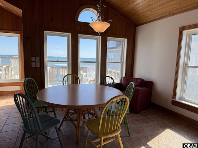 dining room featuring wood ceiling, vaulted ceiling, wood walls, dark tile patterned flooring, and baseboards