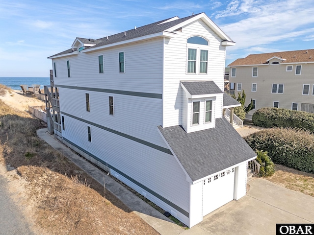 view of property exterior featuring a garage, driveway, a shingled roof, and a water view