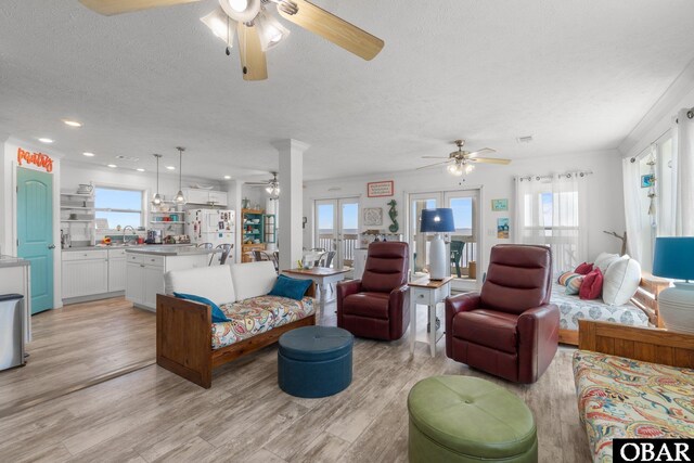 living area featuring light wood finished floors, a ceiling fan, a textured ceiling, and a healthy amount of sunlight