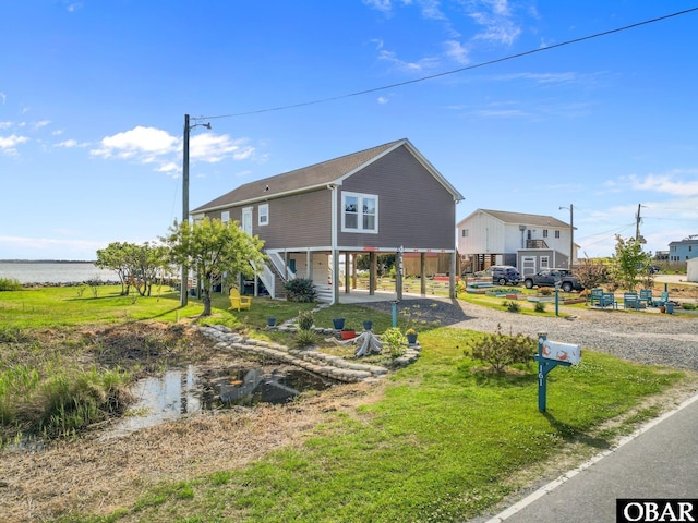 exterior space with stairway, gravel driveway, a front lawn, a water view, and a carport