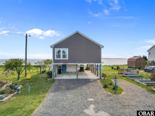 coastal home with a storage shed, an outbuilding, a water view, a front lawn, and gravel driveway