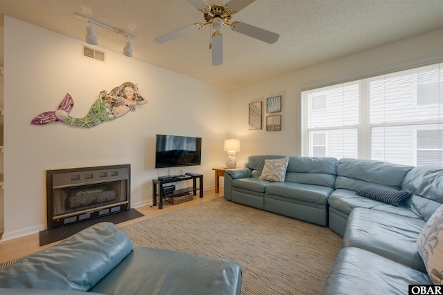 living area with a textured ceiling, a fireplace with flush hearth, wood finished floors, visible vents, and baseboards