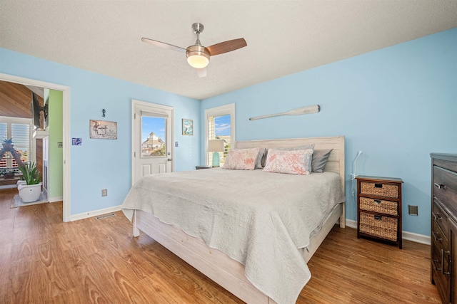 bedroom with a ceiling fan, visible vents, baseboards, and wood finished floors