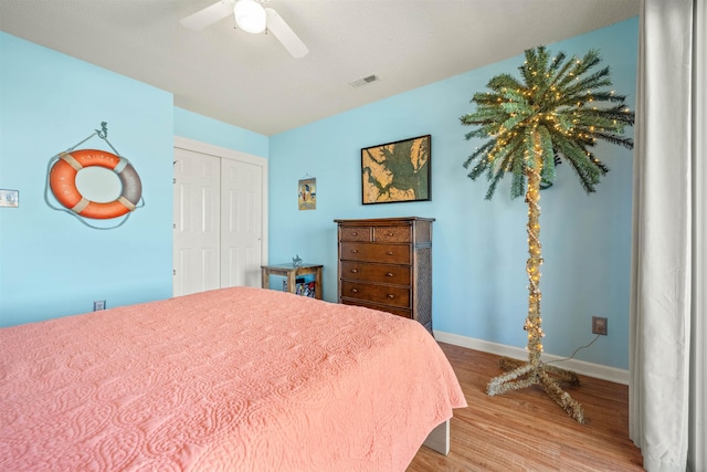 bedroom with a closet, visible vents, a ceiling fan, wood finished floors, and baseboards