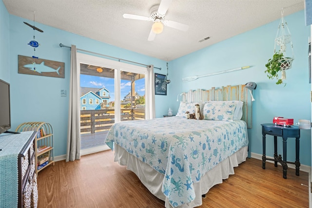 bedroom with access to outside, a textured ceiling, visible vents, and wood finished floors