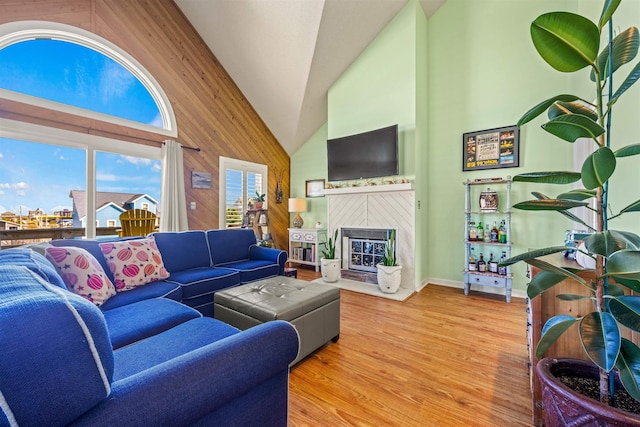 living area with high vaulted ceiling, a fireplace, wooden walls, and wood finished floors