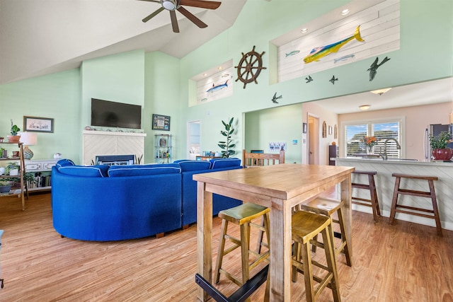 dining space featuring high vaulted ceiling, light wood-type flooring, a fireplace, and ceiling fan