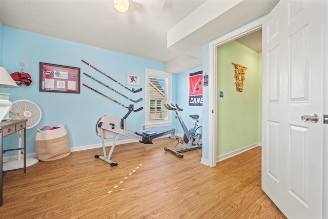 exercise room featuring baseboards and light wood finished floors