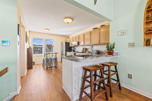 kitchen with light wood-style flooring, backsplash, stainless steel appliances, a kitchen bar, and a sink